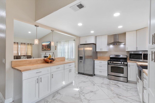 kitchen featuring white cabinetry, vaulted ceiling, wall chimney range hood, pendant lighting, and appliances with stainless steel finishes