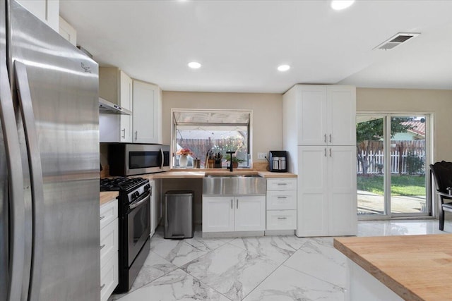 kitchen with white cabinets, stainless steel appliances, wooden counters, and sink