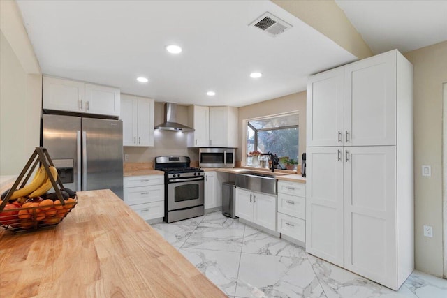 kitchen with sink, wall chimney range hood, white cabinetry, and appliances with stainless steel finishes