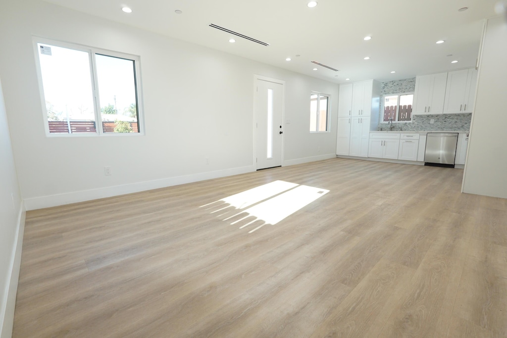 unfurnished living room with light wood-type flooring, a sink, baseboards, and recessed lighting