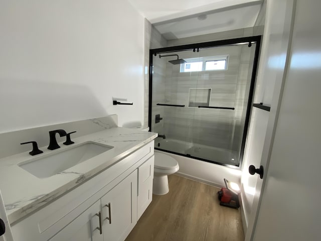 full bathroom with vanity, hardwood / wood-style flooring, shower / bath combination with glass door, and toilet