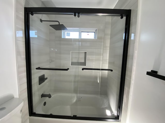 bathroom featuring toilet and combined bath / shower with glass door