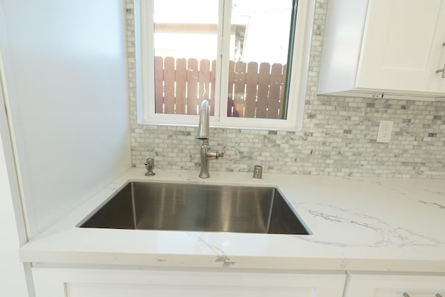 room details with sink, backsplash, white cabinets, and light stone counters