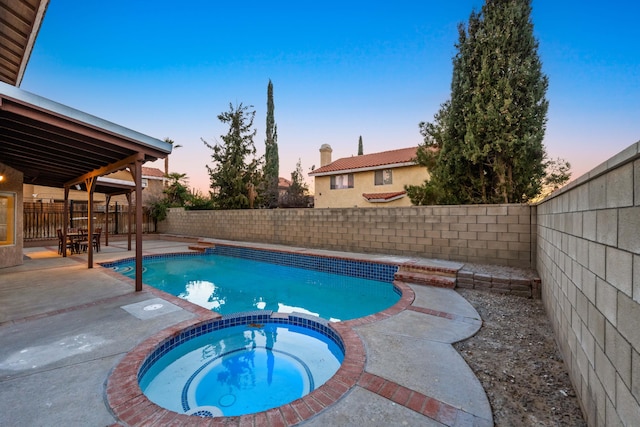 pool at dusk with a patio and an in ground hot tub