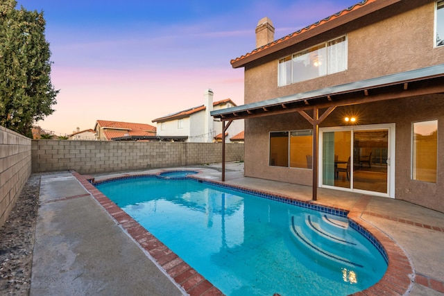 pool at dusk featuring an in ground hot tub and a patio