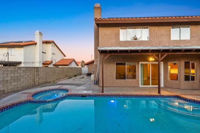 pool at dusk featuring a patio area and an in ground hot tub