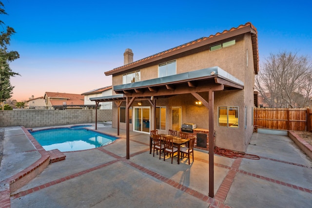 pool at dusk with a grill and a patio area