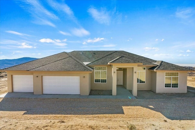 single story home with an attached garage, a shingled roof, and stucco siding