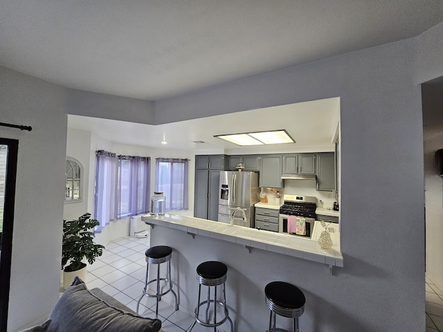 403 Sunrise Ter, Palmdale, CA 93551 - kitchen with a breakfast bar, gray cabinets, stainless steel appliances, tile countertops, and light tile patterned floors