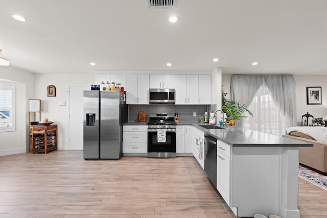 kitchen featuring a peninsula, a sink, appliances with stainless steel finishes, backsplash, and dark countertops