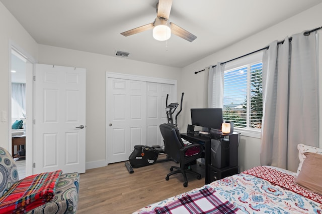 bedroom featuring ceiling fan, wood finished floors, visible vents, baseboards, and a closet