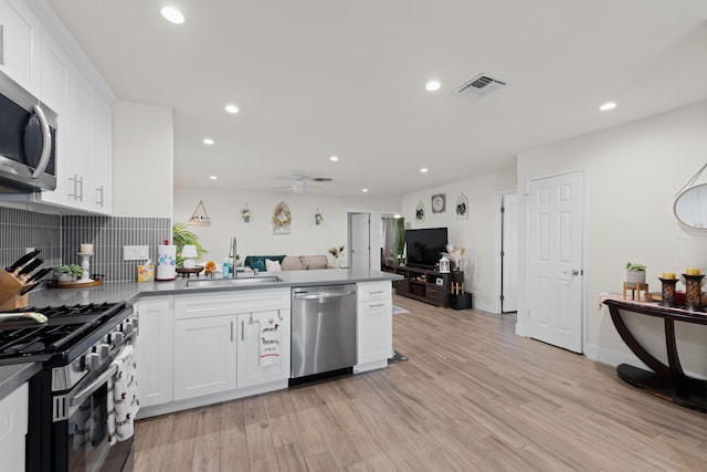 kitchen featuring stainless steel appliances, light wood-style flooring, open floor plan, a sink, and a peninsula