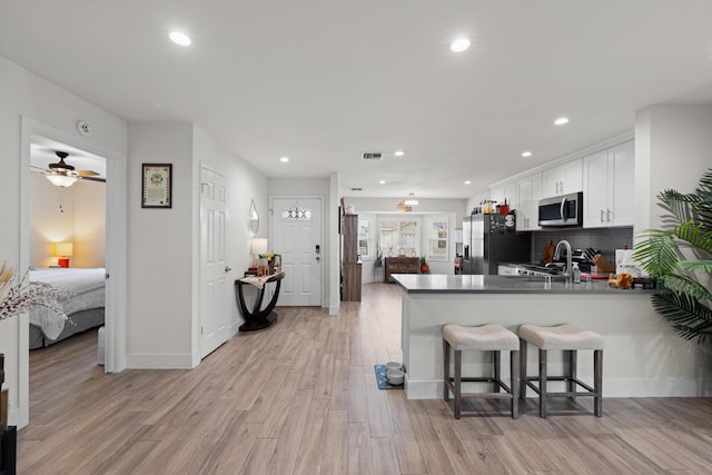 kitchen with stainless steel microwave, light wood-style floors, white cabinets, refrigerator with ice dispenser, and a peninsula