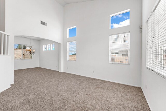 carpeted empty room with a notable chandelier and a high ceiling