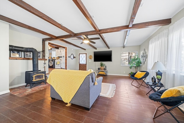 living room featuring beamed ceiling, ceiling fan, and a wood stove