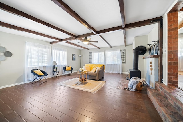 living room with beamed ceiling, dark hardwood / wood-style flooring, a wood stove, and ceiling fan