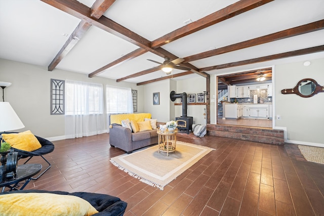 living room featuring beam ceiling, a wood stove, and ceiling fan