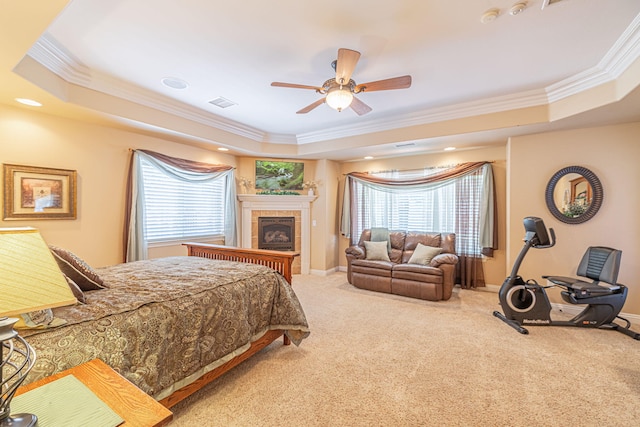 carpeted bedroom with a tray ceiling, a tile fireplace, ceiling fan, and ornamental molding