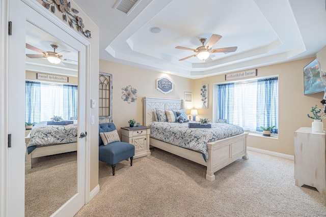 bedroom with a raised ceiling, ceiling fan, and light carpet