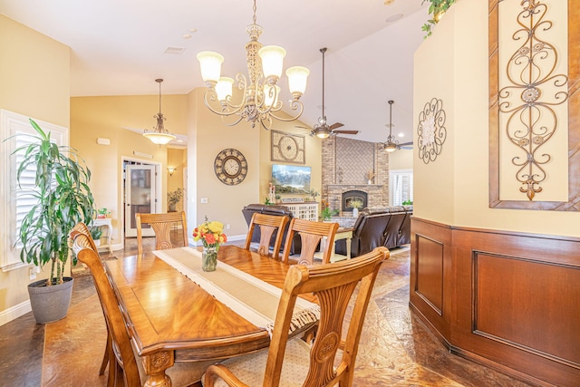 dining space with ceiling fan with notable chandelier, vaulted ceiling, and a brick fireplace