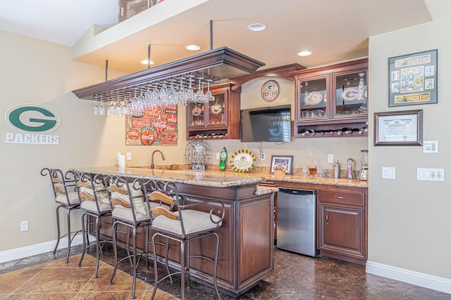 bar featuring light stone counters, sink, and refrigerator