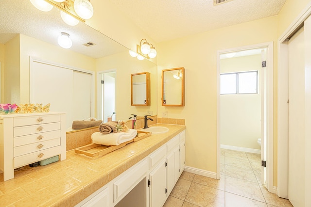 bathroom with a textured ceiling, visible vents, baseboards, and vanity