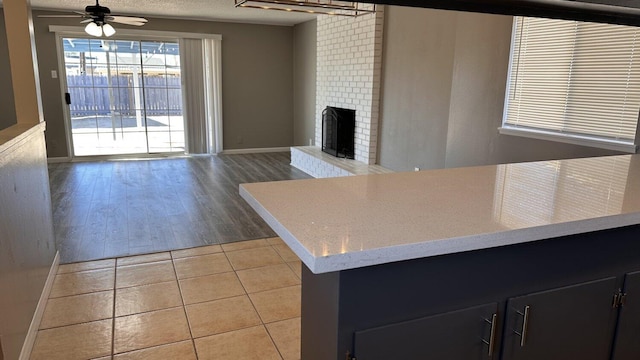 kitchen with ceiling fan, a brick fireplace, light tile patterned floors, and a textured ceiling