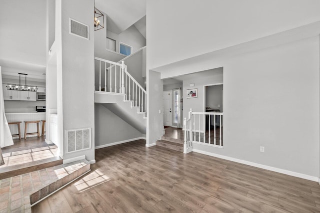 unfurnished living room with hardwood / wood-style flooring, a towering ceiling, and an inviting chandelier