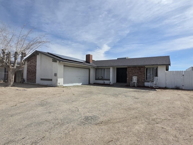 view of front facade with brick siding, stucco siding, an attached garage, roof mounted solar panels, and fence