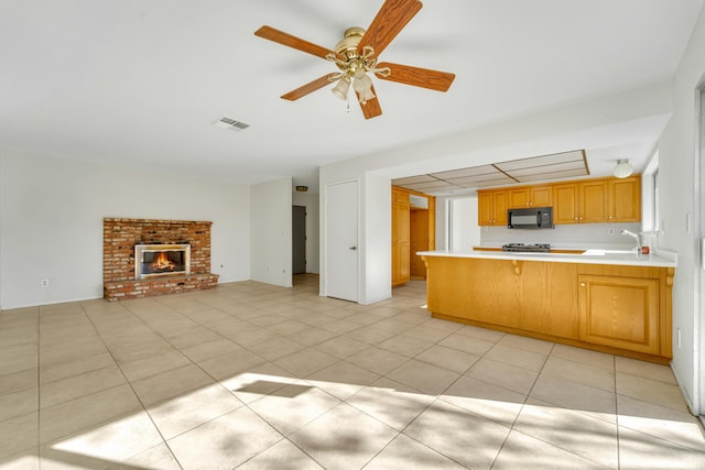 kitchen with kitchen peninsula, a brick fireplace, ceiling fan, sink, and light tile patterned floors