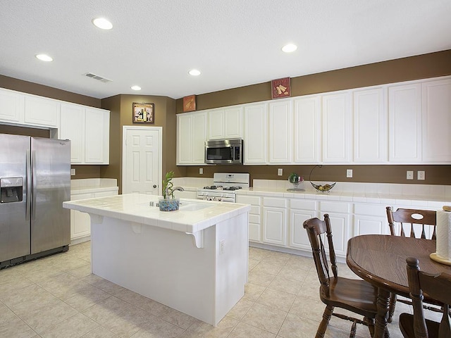 kitchen featuring white cabinetry, a center island with sink, stainless steel appliances, tile countertops, and visible vents