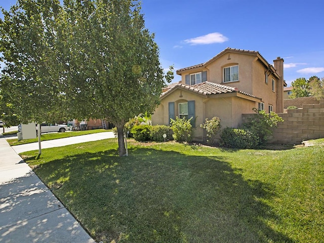 view of front facade with a front yard, stucco siding, a tile roof, and fence