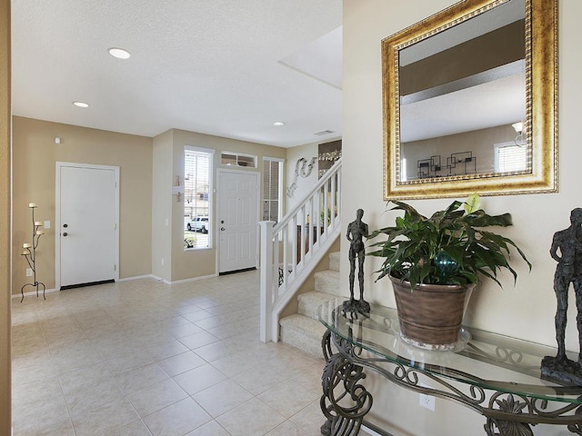 entryway with a textured ceiling, baseboards, stairs, recessed lighting, and tile patterned flooring