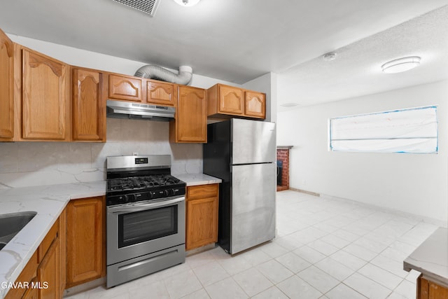 44338 W 23rd St, Lancaster, CA 93536 - kitchen with appliances with stainless steel finishes, under cabinet range hood, light stone countertops, brown cabinetry, and backsplash