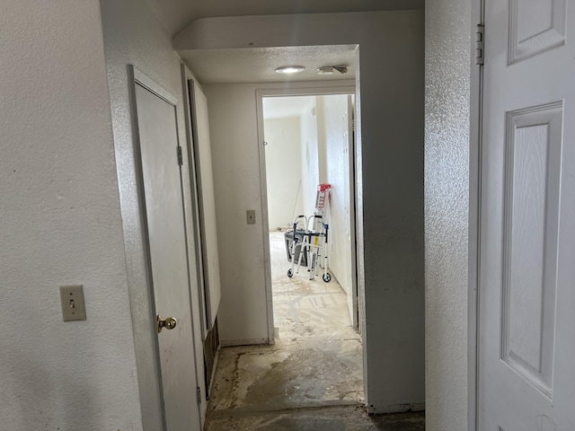 hallway featuring unfinished concrete flooring and a textured wall