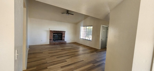 unfurnished living room with dark hardwood / wood-style flooring, a brick fireplace, a textured ceiling, vaulted ceiling, and ceiling fan