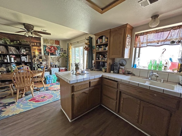 kitchen featuring a ceiling fan, a textured ceiling, a peninsula, tile countertops, and dark wood-style flooring
