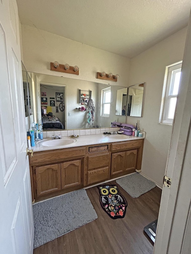 bathroom with ensuite bathroom, a textured ceiling, double vanity, wood finished floors, and a sink