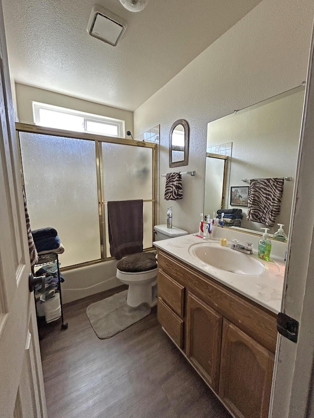 bathroom with shower / bath combination with glass door, vanity, toilet, a textured ceiling, and wood finished floors