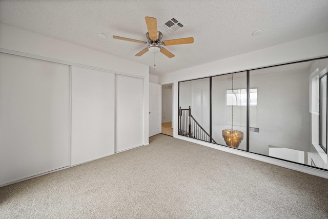 unfurnished bedroom with a ceiling fan, visible vents, carpet floors, a closet, and a textured ceiling