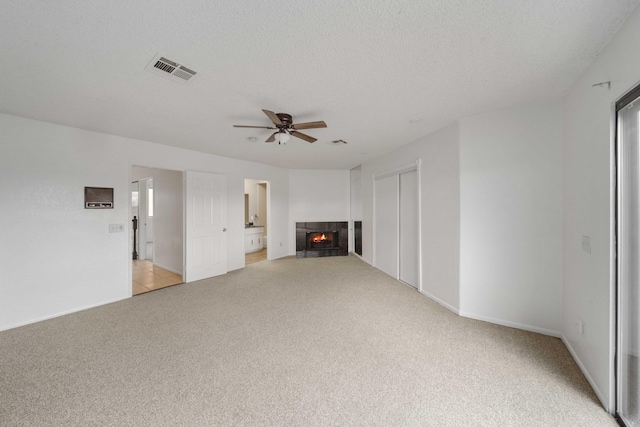 unfurnished living room featuring visible vents, a tiled fireplace, a textured ceiling, light colored carpet, and ceiling fan