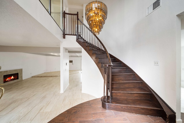 stairs featuring visible vents, an inviting chandelier, a fireplace, and a towering ceiling