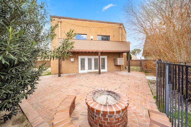 rear view of house featuring stucco siding, a patio, an outdoor fire pit, fence, and a balcony