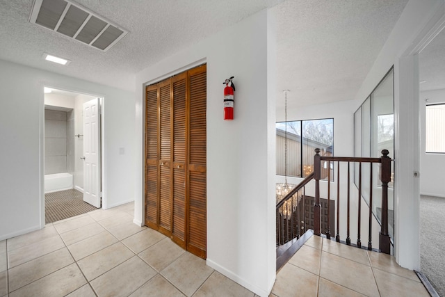 hallway with light tile patterned floors, baseboards, visible vents, a textured ceiling, and an upstairs landing