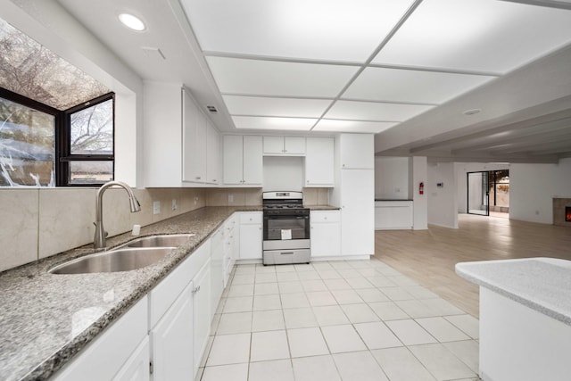 kitchen featuring a sink, backsplash, gas range oven, white cabinets, and light tile patterned floors