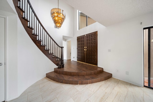 foyer with marble finish floor, a textured ceiling, stairway, a high ceiling, and a chandelier