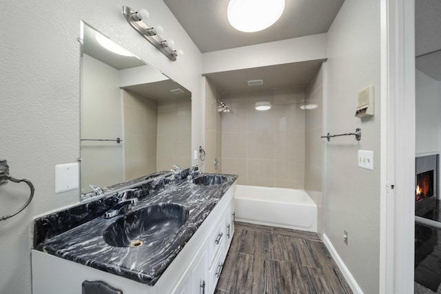 full bathroom featuring baseboards, wood tiled floor, shower / bath combination, a lit fireplace, and vanity