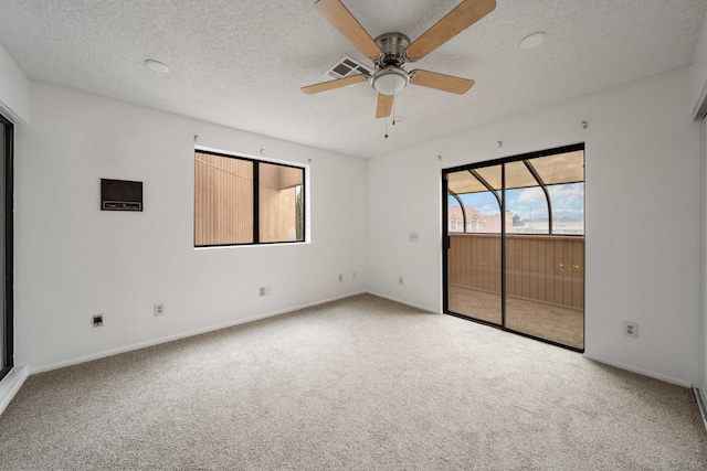 carpeted empty room with a textured ceiling, baseboards, visible vents, and ceiling fan