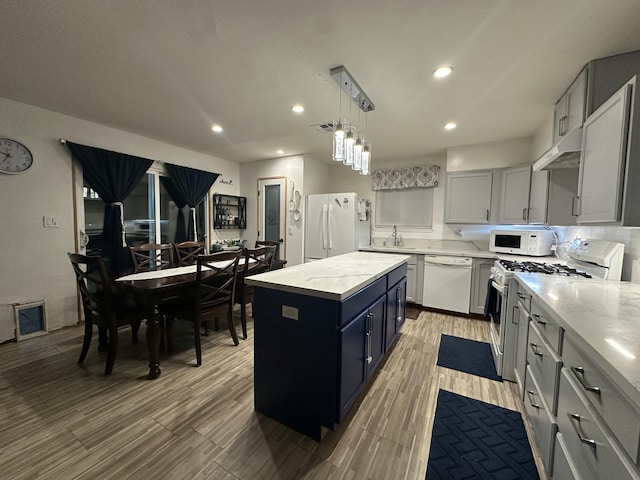 kitchen featuring decorative light fixtures, white appliances, a center island, and light stone countertops