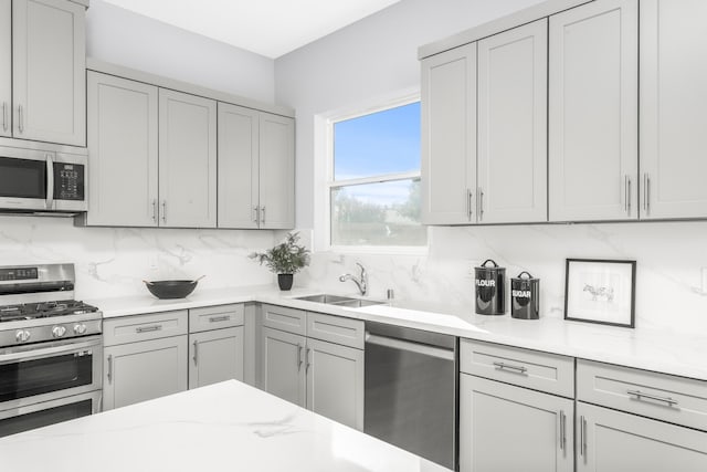 kitchen featuring sink, gray cabinetry, stainless steel appliances, light stone countertops, and decorative backsplash